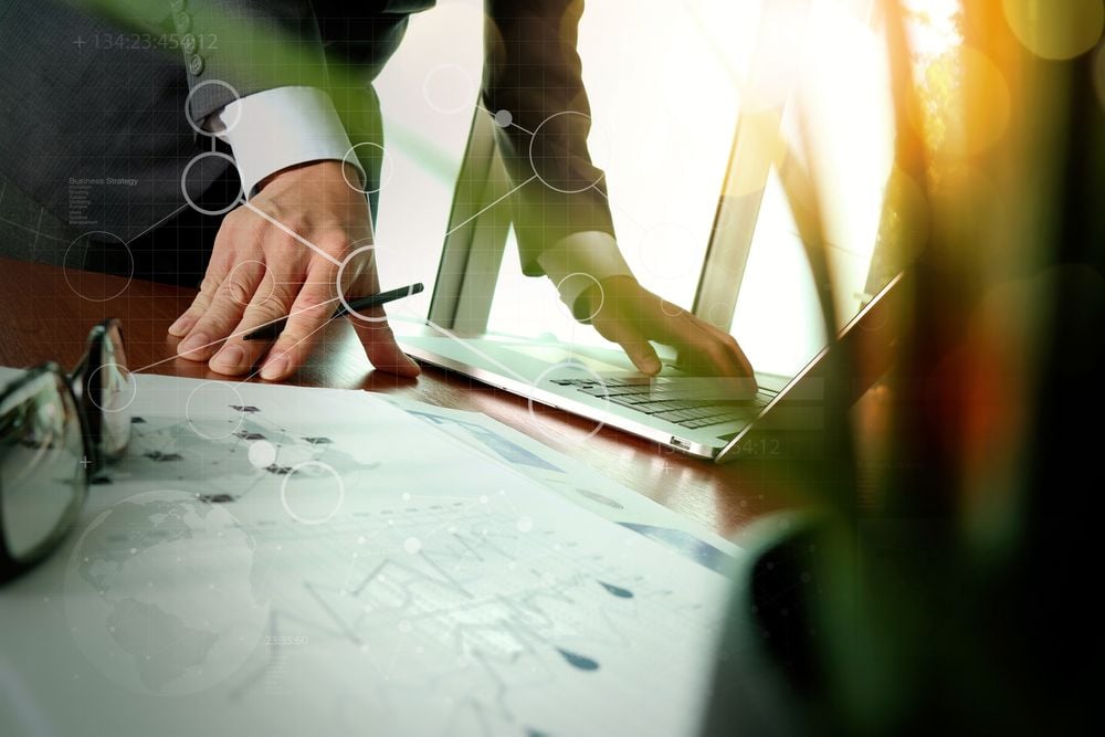 businessman hand working with new modern computer and business strategy documents digital layers with green plant foreground on wooden desk in office